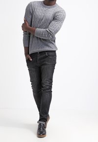 Pull en laine gris à maille torsadée avec manches longues, associé à un jean slim foncé et des chaussures noires à enfiler avec une semelle marron. Design simple et texturé.