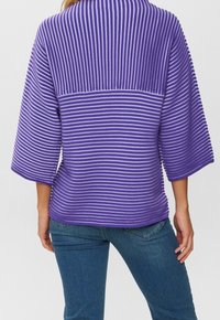 Person, der einen lila und weißen, horizontal gestreiften Pullover mit 3/4-Ärmeln und blauen Jeans trägt, von hinten gezeigt.