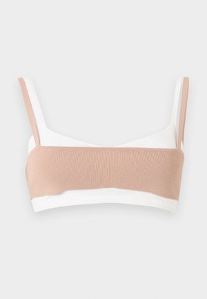 Αόρατο λευκό bralette με πλατιά πλεκτή λωρίδα ανοιχτού μπεζ χρώματος στο μπροστινό μέρος και ταιριαστά μπεζ τιραντάκια σε απλό φόντο.