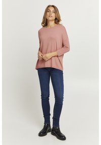 Rózsaszín hosszú ujjú felső kerek nyakkivágással, laza szabással és puha textúrával, sötét skinny farmernadrággal és fekete bokacsizmával párosítva.