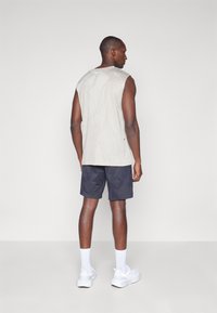Top sin mangas de color gris claro con un patrón texturizado, combinado con pantalones cortos oscuros de color azul marino con diseños geométricos y zapatillas deportivas blancas.