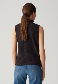 Black sleeveless top with a textured design, high neckline, and a relaxed fit, paired with blue jeans featuring a standard five-pocket style.