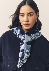 Lightweight scarf featuring a blue and black abstract pattern, soft texture, and a long rectangular shape, draped elegantly around the neck.