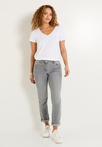 Camiseta blanca de cuello en V combinada con pantalones de mezclilla gris claro con dobladillo. El conjunto se complementa con zapatillas blancas de diseño sencillo.
