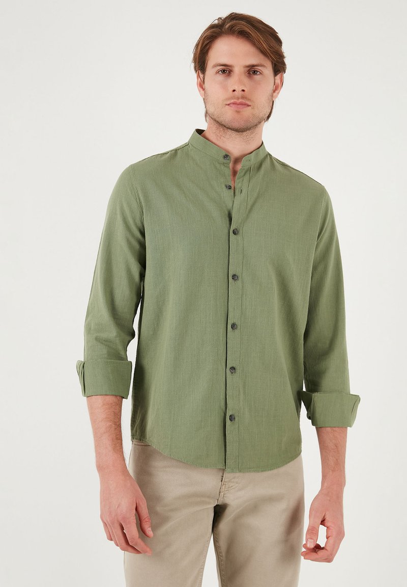 Chemise olive verte à col, à manches longues, avec fermeture à bouton et poignets retroussés, présentant un tissu texturé et un ourlet droit.