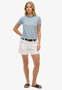 Gestreepte korte mouwen T-shirt in blauw en wit, gecombineerd met witte denim short met rafelige zoom, en zwarte slip-on sandaal. Zwarte riemaccent.
