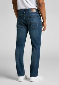Jeans in denim blu con una vestibilità dritta, caratterizzati da un'etichetta in pelle marrone con il logo Lee sulla cintura e due tasche posteriori.