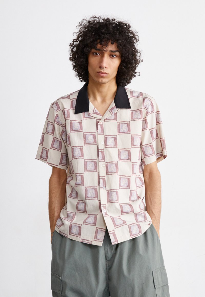 Short-sleeve button-up shirt in cream with maroon square pattern and black collar. Lightweight fabric, relaxed fit, visible buttons.