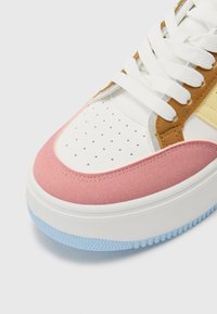Baskets multicolores avec une tige en cuir blanc, des accents en daim rose, des superpositions marron et jaunes, et une semelle en caoutchouc texturée bleue.