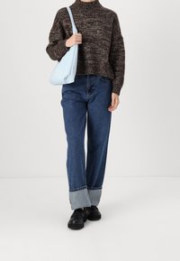 Brauner Strickpullover mit hohem Kragen, kombiniert mit weitem, blauen Jeans mit einem karierten Saum. Schwarze Schuhe und eine hellblaue Umhängetasche.
