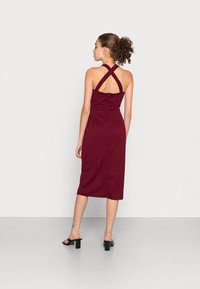 Vestuário midi em borgonha com textura canelada, design de costas cruzadas, silhueta ajustada e costuras verticais. Apresenta um fecho oculto nas costas.