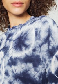 Marinblå och vit tie-dye tröja med texturerad stickning, vågformad halsringning och en avslappnad passform, med framträdande virvlande mönster.