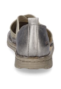 Metalicznie srebrna tylna część sandała, z miękką, tanową wyściółką, teksturowaną beżową podeszwą i przeszywaną szwem detalem wzdłuż tyłu.