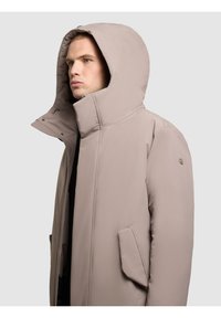 Světlé béžové zateplené sako s vysokým límcem, velkou kapucí a dvěma bočními kapsami. Disponuje hladkým materiálem a aerodynamickým designem.