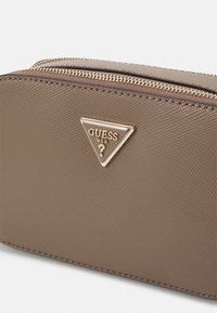 Borsa sintetica marrone con texture e finiture in oro, caratterizzata da un logo triangolare con la scritta "GUESS USA." Chiusura con cerniera lungo la parte superiore.