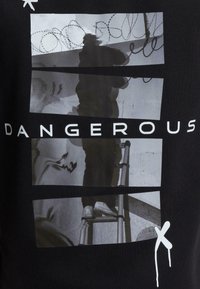 Fekete grafikai póló, amely fekete-fehér képek kollázsát ábrázolja, és a "DANGEROUS" feliratot tartalmazza vastag fehér betűkkel.