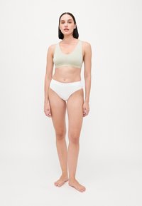 Bralette verde claro sem costura com alças largas e decote profundo, combinado com roupa interior branca de cintura alta, ambos em um tecido suave.