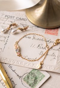 Auksinis apyrankė su gėlių motyvais ir pastelinių atspalvių akcentais. Švelni grandinėlė, homarinis užsegimas ir mažas pakabukas. Kartu su perlų pakabinamiais auskarais.