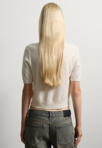 Suéter de crema de manga corta con un diseño ajustado y dobladillo acanalado, combinado con jeans de tiro alto de color azul desgastado que tienen bolsillos traseros.