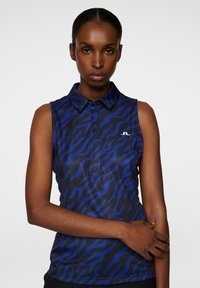 Sleeveless polo shirt in dark blue with black tiger stripe pattern, featuring a collared neck and a small white logo on the chest.