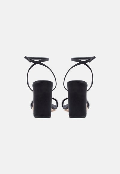 Μαύρα σανδάλια με ψηλό τακούνι πλακέ, λουράκια στον αστράγαλο που διασταυρώνονται στο πίσω μέρος και λουράκια στα δάχτυλα διακοσμημένα με στρας.