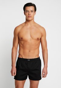 Schwarze Badeshorts mit elastischem Bund und einem dezenten Logo auf der Vorderseite, das ein schlichtes und funktionales Design präsentiert.