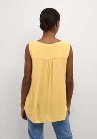 Sleeveless yellow blouse made of lightweight fabric, featuring a round neckline and subtle pleat detail at the back.