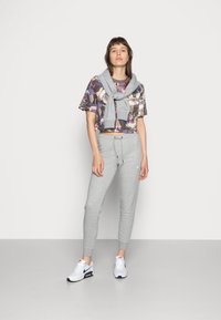 Un pantalon de jogging gris avec des chevilles resserrées, un t-shirt court à motifs floraux violets, roses et blancs, et un pull gris noué autour des épaules.