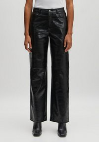 Schwarze Kunstleder-Hosen mit weitem Bein und Kroko-Optik, mit vorderen Taschen und hoher Taille, kombiniert mit Stiefeletten.