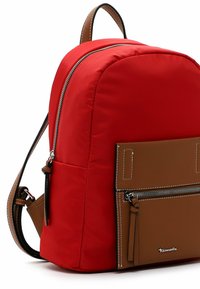 Sac à dos en nylon rouge avec des accents en cuir brun, poche zippée à l'avant et détails texturés. Bretelles ajustables et quincaillerie métallique visibles.