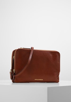 Sac bandoulière en cuir marron avec logo doré. Dispose d'une fermeture éclair et d'une sangle ajustable. Texture lisse avec un design minimaliste.