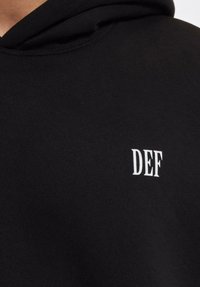 Czarna bluza z kapturem z białym haftowanym napisem "DEF" na lewej piersi, wykonana z miękkiego, teksturowanego materiału, z kieszenią typu kangur.