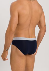 Marineblauwe slips van zacht materiaal met een grijze elastische tailleband met het "Hanro"-logo. Glad textuur, strakke pasvorm.