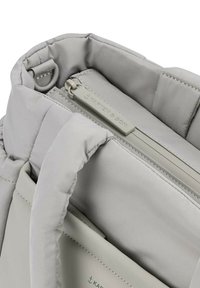 Borsa a spalla imbottita grigia chiara in tessuto morbido, con tasca con zip e etichetta logo. Presenta manici robusti e dettagli di cucitura discreti.