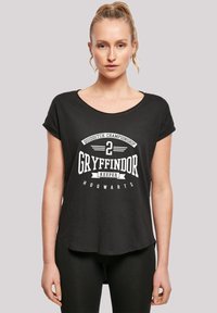 Svart T-skjorte med korte ermer og rund hals, med hvit tekstdesign som sier "Quidditch Championship 2 Gryffindor Keeper Hogwarts."