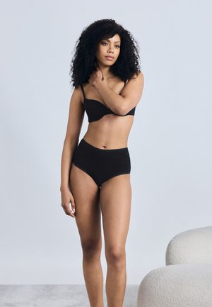 Zwarte lingerie set bestaande uit een beha met dunne bandjes en tailleslippende slips. Glad stof met gegolfde randen en een minimalistisch ontwerp.