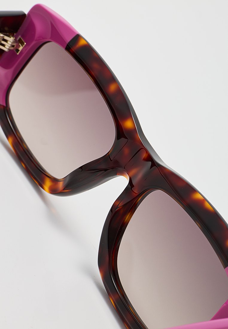 Übergroße Sonnenbrille mit einem Schildpatt-Rahmen und rosa Akzenten. Übergangslinsen und ein glatter, glänzender Finish. Auffällige, markante Form.