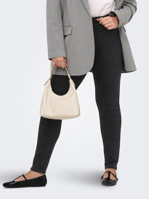 Person trägt ein graues Nadelstreifen-Sakko, schwarze Skinny-Jeans, schwarze Ballerinas und hält eine kleine beige Handtasche am kurzen Henkel.
