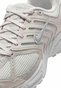 Ljusgrå sportskor med mesh- och mockamaterial, med en silverfärgad swoosh-logotyp, texturerade accenter och snörningssystem för en säker passform.