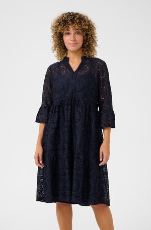 Robe en dentelle bleu marine avec un décolleté en V, des manches trois-quarts et un ourlet en couches, présentant des motifs floraux et une coupe décontractée.