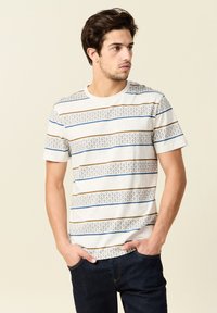 Lyhythihainen, pyöreäkauluksinen t-paita heather-harmaana, jossa on vaaleanruskeita ja sinisiä vaakaraitoja. Paidan helmaa koristaa kuvioitu raidalinja.