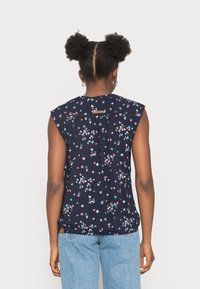 Blusa sem mangas azul marinho com um estampado de borboletas florais em rosa e turquesa; apresenta um costas franzidas e um pequeno rótulo perto do pescoço.