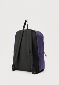 Sac à dos violet et noir avec bretelles rembourrées, poignée de transport et poche latérale, montré de dos sur un fond uni.