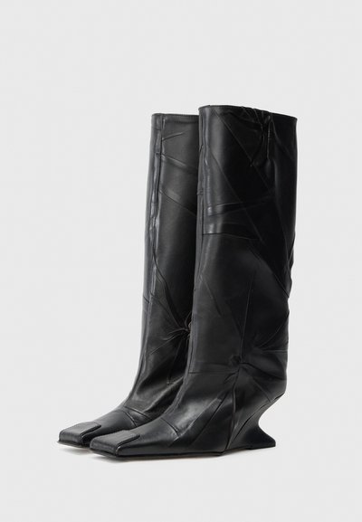 Melnas ādas zābaki ar augstu, konisku siluetu. Raksturīgas leņķainas locījumi, kvadrātveida purngali un konturēts šķērseniskais papēdis. Gluda tekstūra.