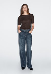 Hnědý krátký rukáv top spárovaný s tmavě modrými, vysokým pasem širokými džíny. Oblečení má klasický design s hladkou texturou.