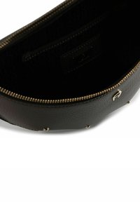 Interior de bolso de cuero negro texturizado, con cierre de cremallera, herrajes en tono dorado y un pequeño bolsillo para organización.