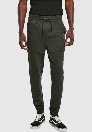 Mørkegrå sweatpants med snørresnor i taljen, tapered ben og detaljer i sidelapper, båret med sorte og hvide sneakers.