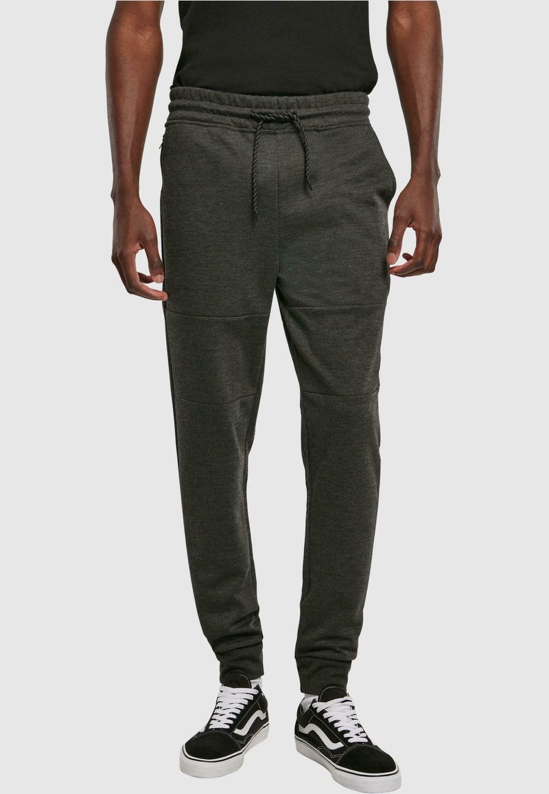 Donkergrijze sweatpants met een trekkoord in de taille, taps toelopende benen en details in de zijkanten, gecombineerd met zwart-witte sneakers.