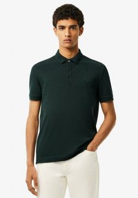 Mörkgrön pikétröja med slim fit, korta ärmar och krage. Har en knappslå och en liten logotyp på bröstet. Strukturerad tyg.
