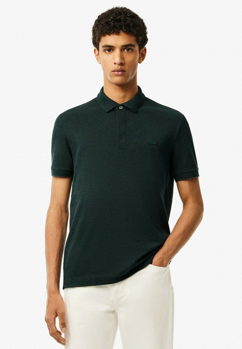 Mörkgrön pikétröja med slim fit, korta ärmar och krage. Har en knappslå och en liten logotyp på bröstet. Strukturerad tyg.